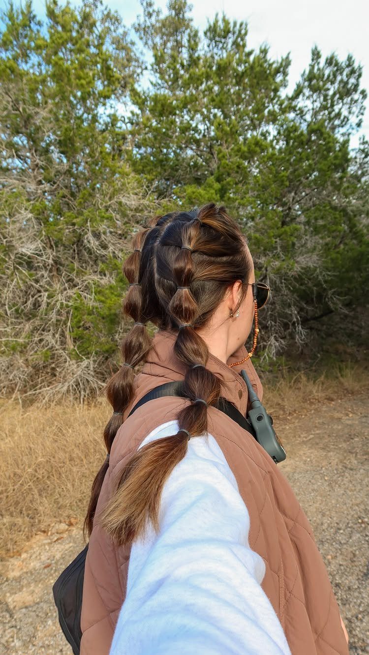 12 Braids Hairstyles: 29 Ideas, From Box Braids to Milkmaid 29 Woman with brown hair styled in a bubble braid ponytail outdoors in nature.