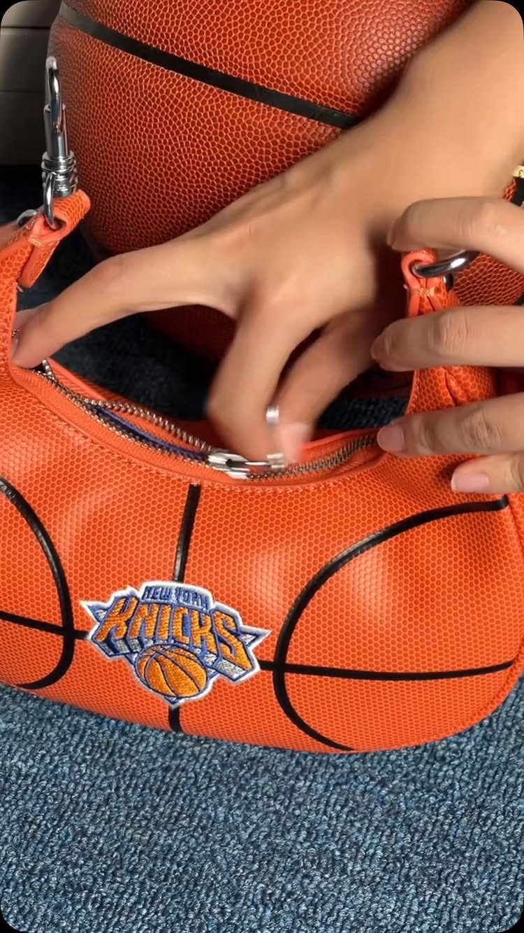 Orange basketball-shaped handbag with New York Knicks logo held by a person's hands.