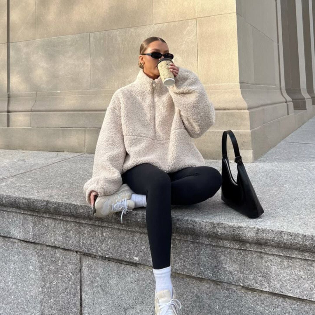 Woman in beige fleece pullover and black leggings sitting on stone steps.