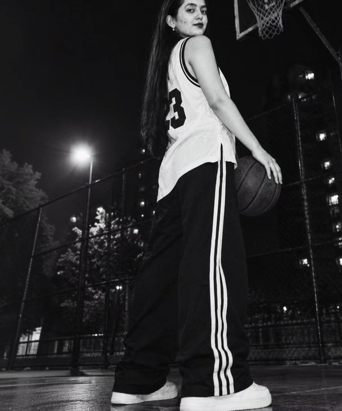 Woman in basketball jersey and striped athletic pants holding a ball on court