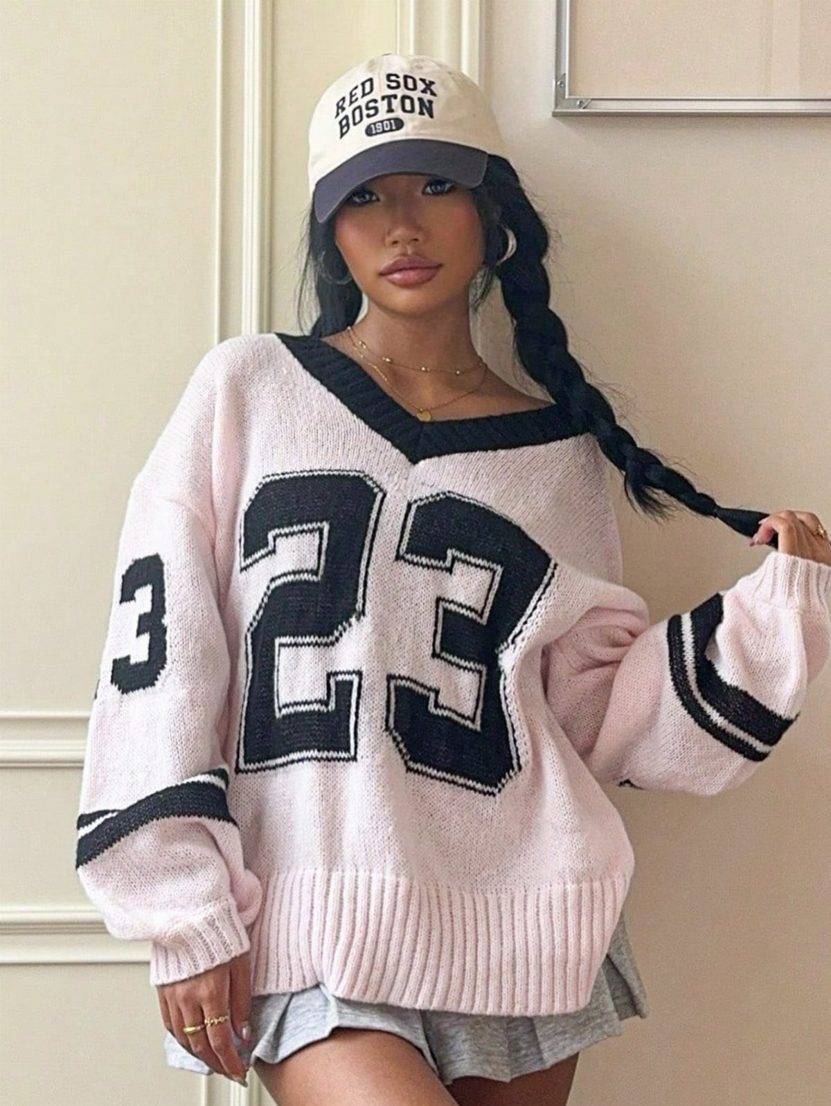Woman in a pink oversized number 23 knit sweater and baseball cap.