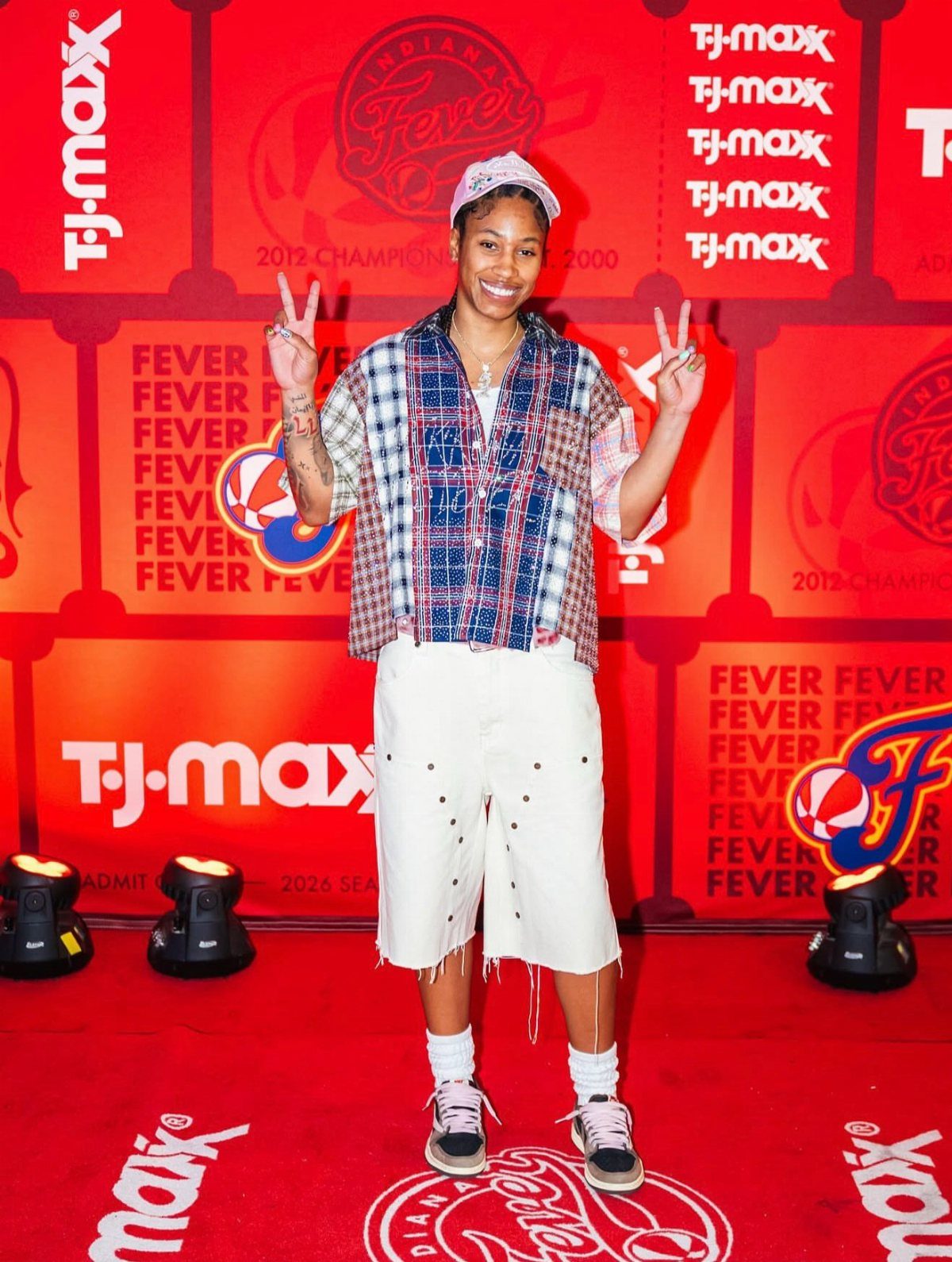 Woman in a blue plaid shirt and white frayed shorts posing on red carpet.