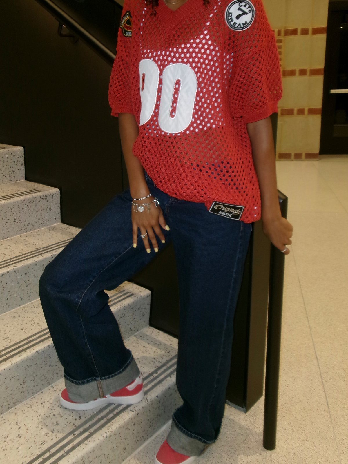 Person wearing a red mesh basketball jersey, wide-leg blue jeans, and red sneakers.