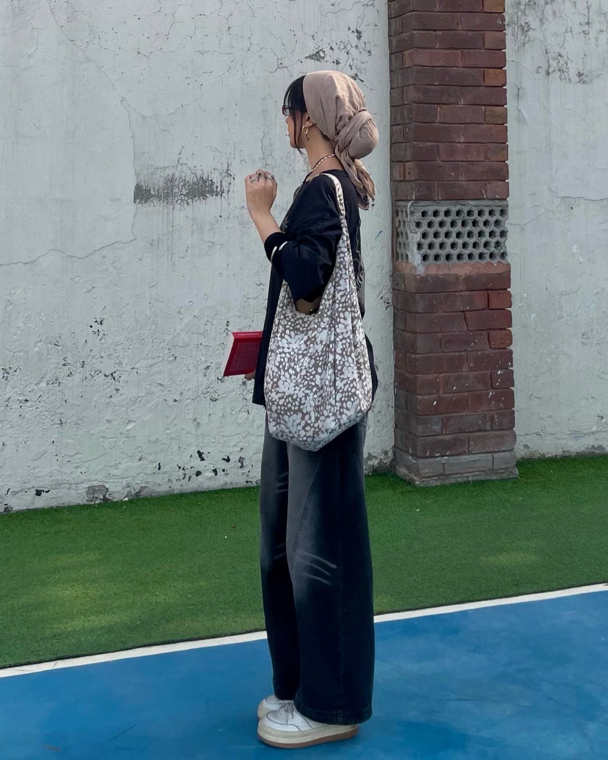 Woman in black button-down shirt and baggy black pants with a beige headscarf.