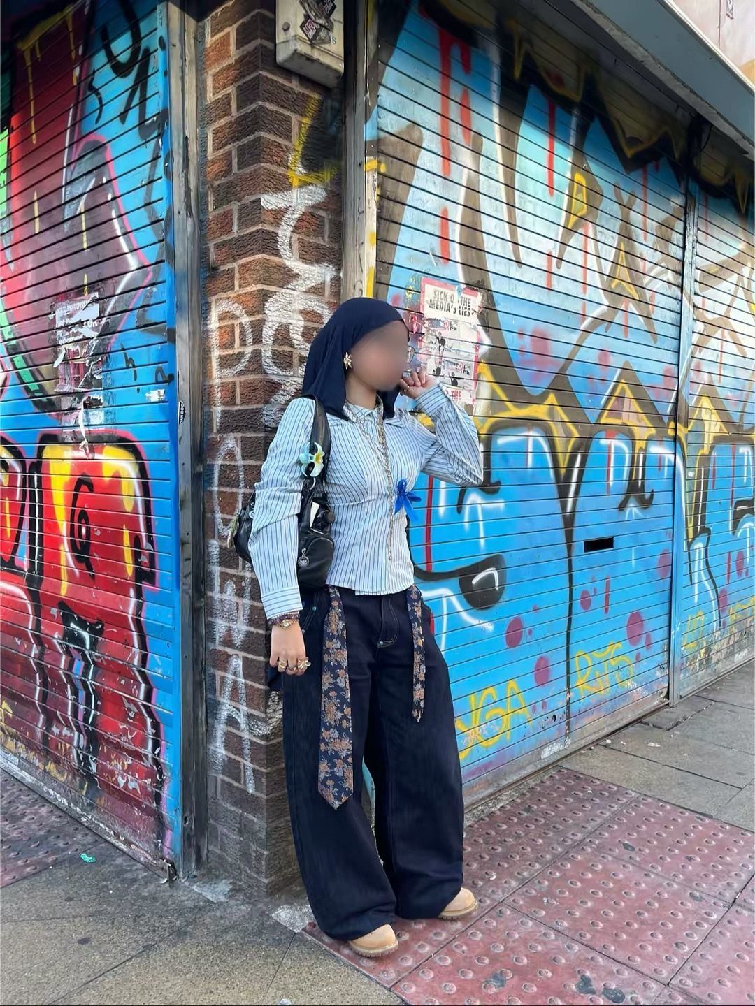 Woman in striped shirt and black baggy pants posing against graffiti wall