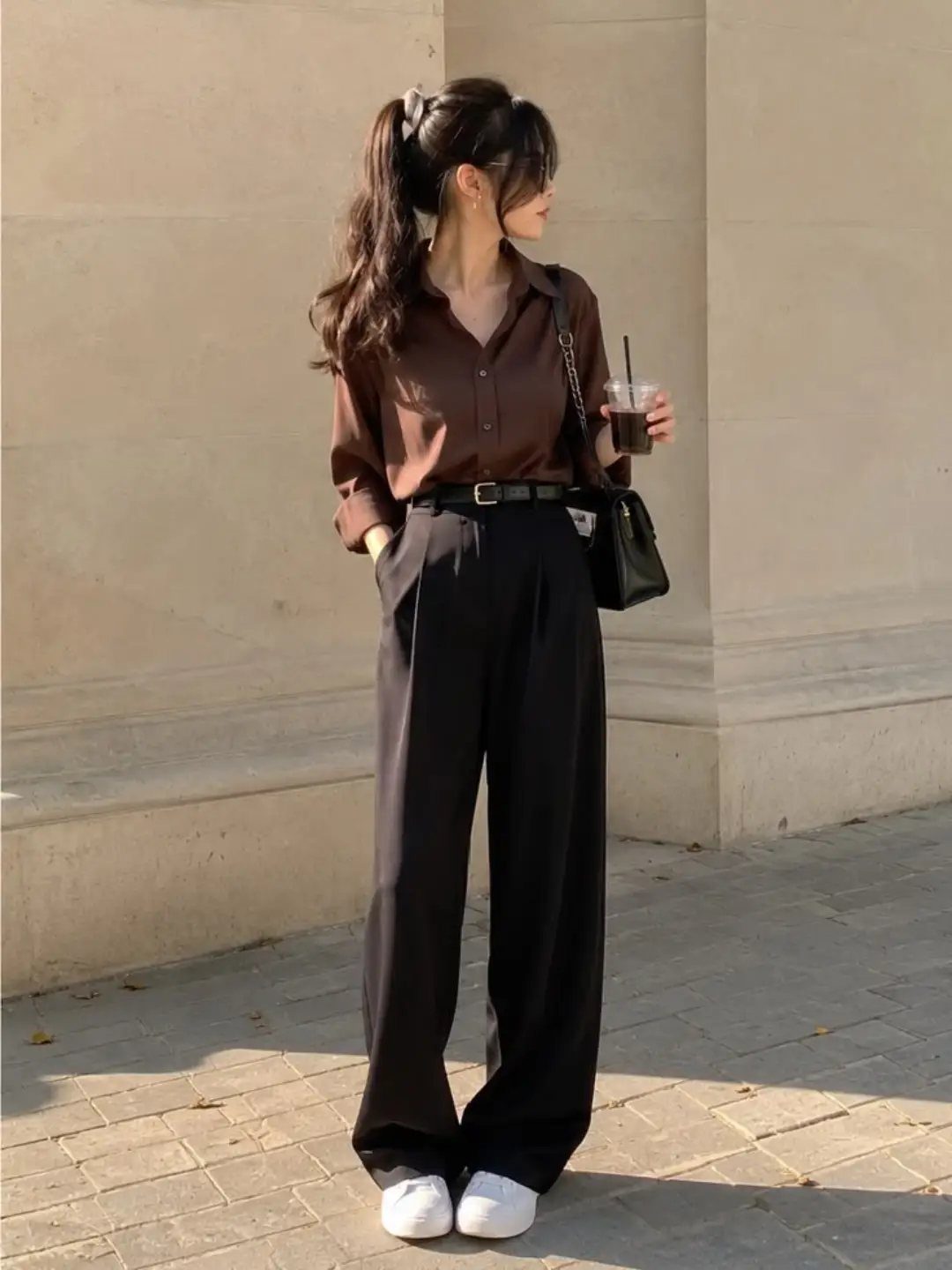 Woman wearing a brown button-down shirt and black baggy trousers with white sneakers.