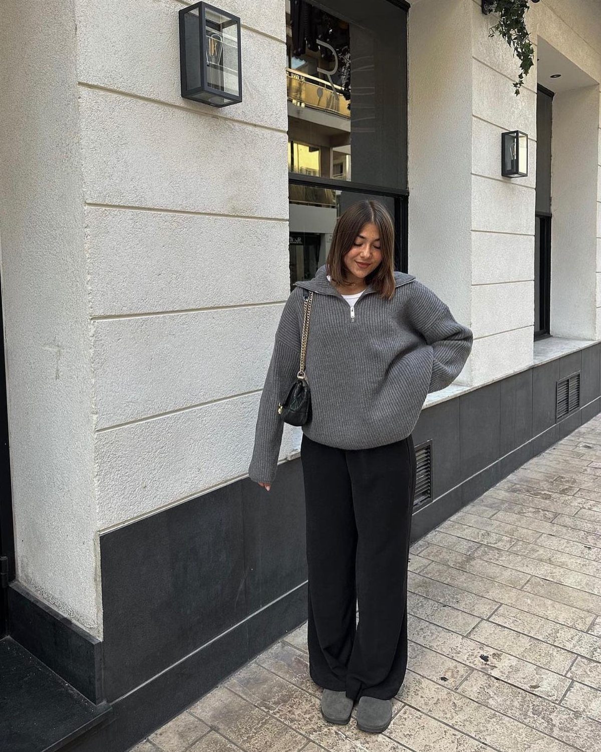 Woman wearing a dark grey oversized sweater and wide-leg black pants on a sidewalk.