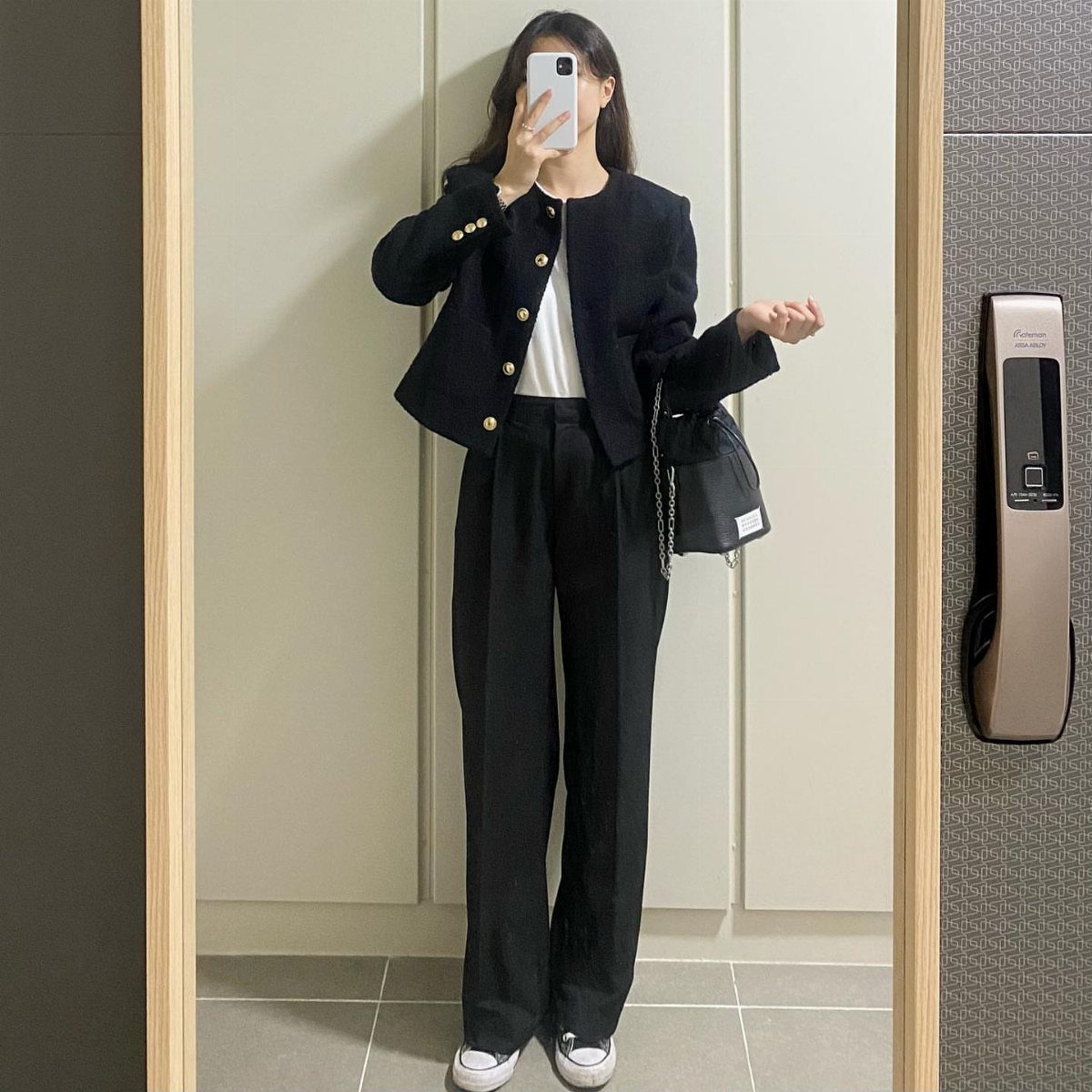 Woman in navy buttoned jacket and black baggy trousers taking a mirror selfie.