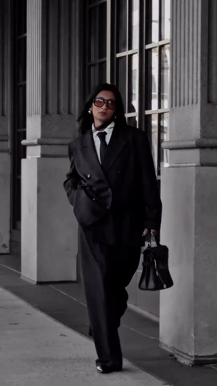 Woman in oversized black double-breasted blazer and wide-leg black trousers with a black handbag