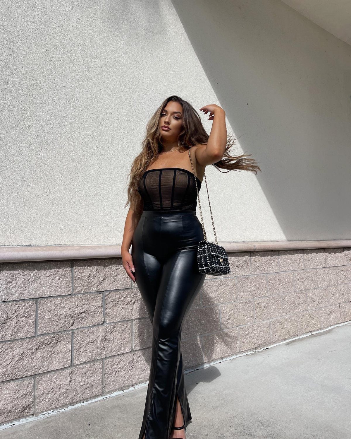 Woman wearing a black strapless corset and black leather trousers posing outdoors.