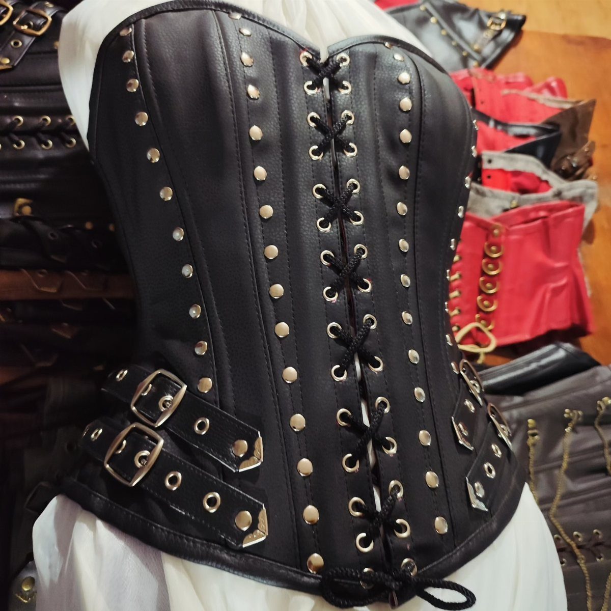 Black leather corset with silver studs and buckled straps on a white mannequin.