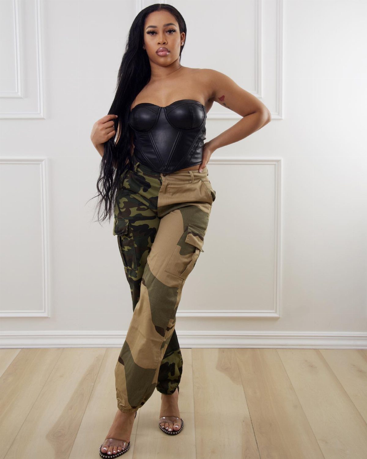 Woman wearing a black leather corset and camouflage cargo pants posing in a room.