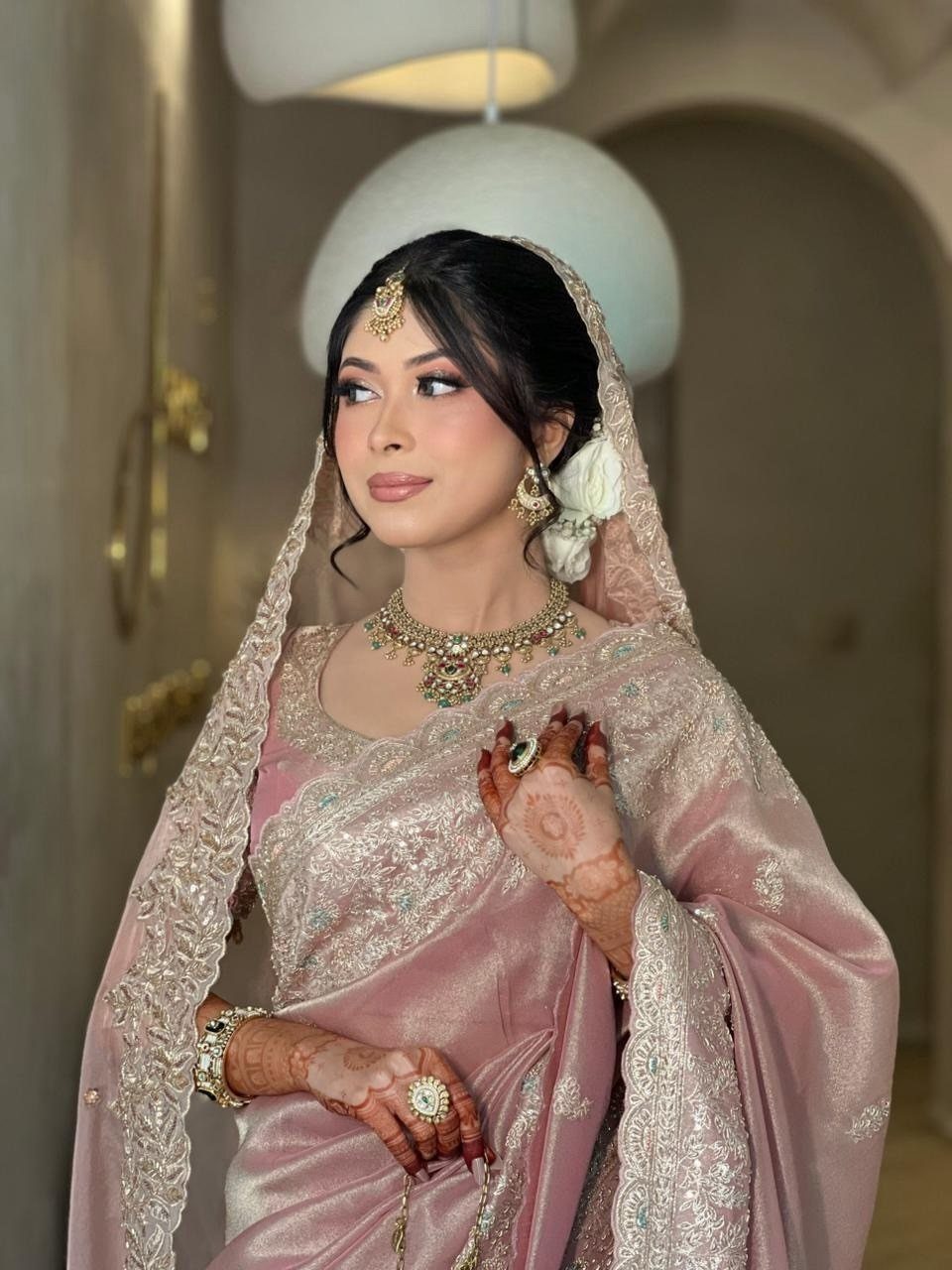 25 Blush Wedding Dress Ideas in Lace, Tulle, Silk and Sequins 20 Woman in a blush pink embroidered bridal saree and gold jewelry posing indoors.