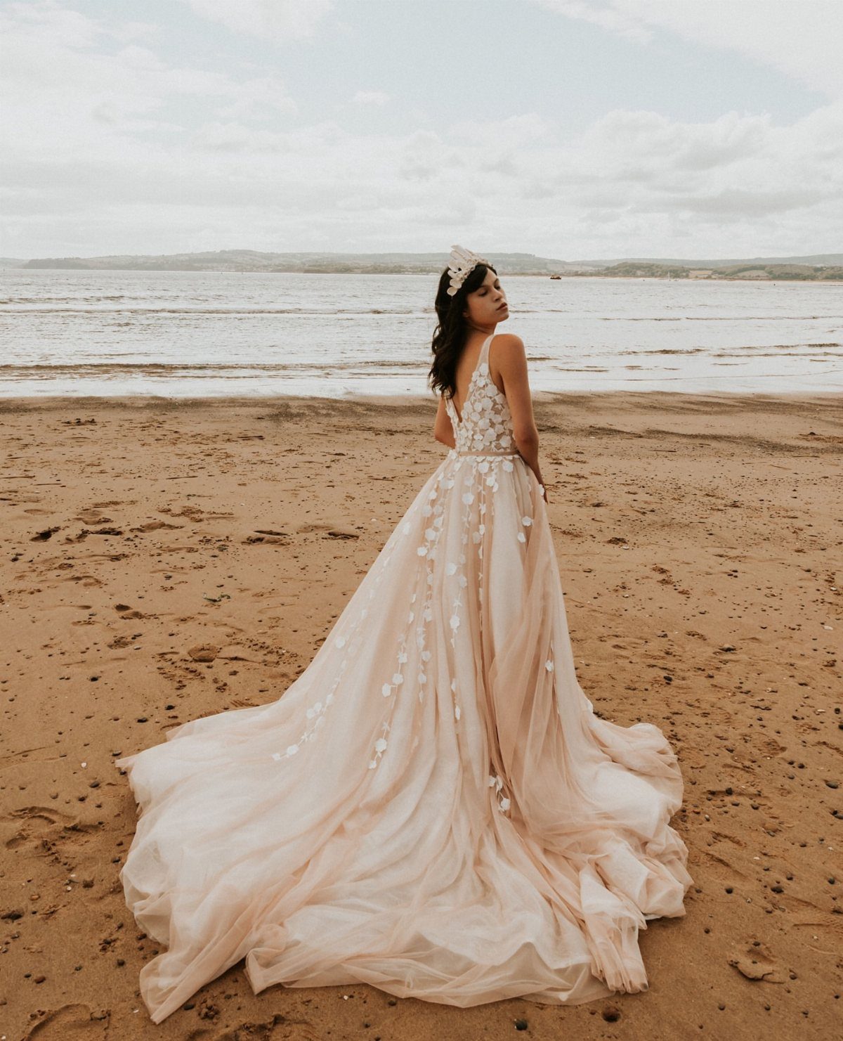 25 Blush Wedding Dress Ideas in Lace, Tulle, Silk and Sequins 17 Woman in a blush floral gown with a long train on a sandy beach