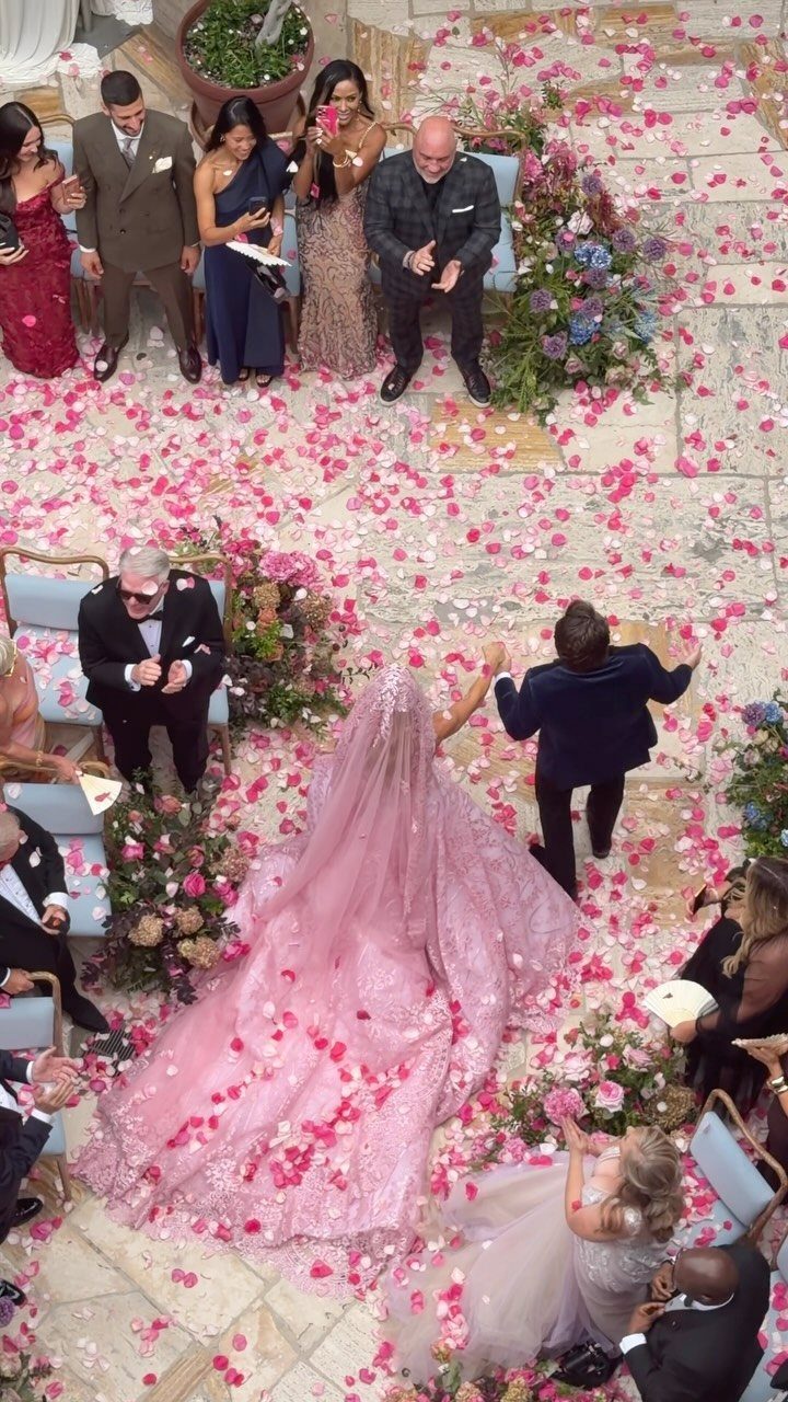 25 Blush Wedding Dress Ideas in Lace, Tulle, Silk and Sequins 15 Bride in a voluminous light pink gown walking on a petal-covered stone path