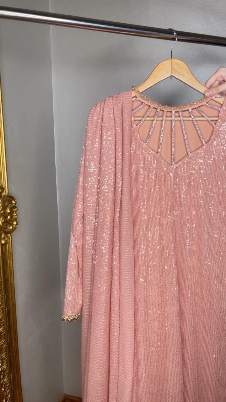 25 Blush Wedding Dress Ideas in Lace, Tulle, Silk and Sequins 6 Blush pink long-sleeved sequin gown hanging on a wooden hanger from a rack.
