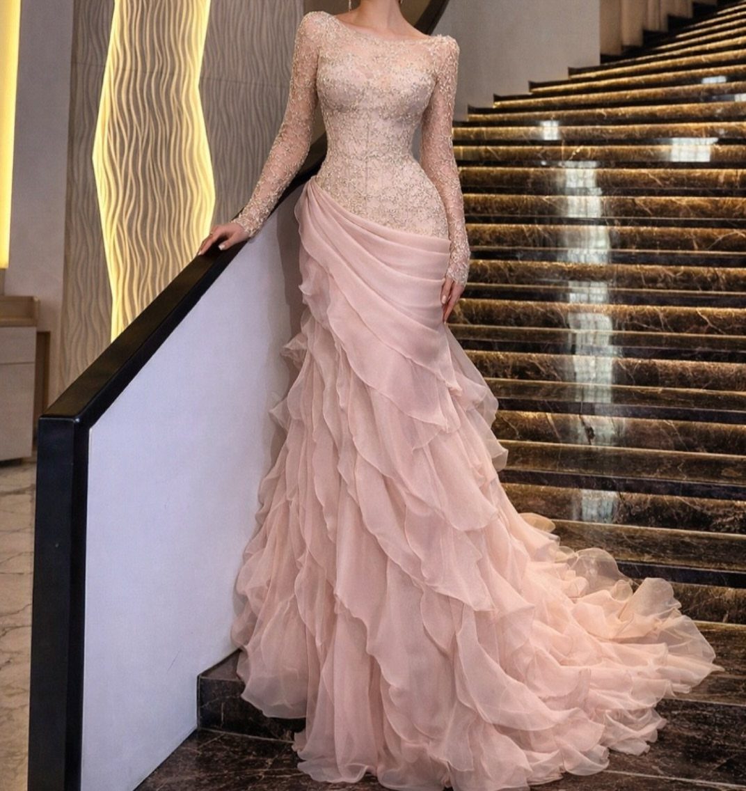 25 Blush Wedding Dress Ideas in Lace, Tulle, Silk and Sequins 5 Woman in a peachy-pink gown with a tiered ruffled skirt on marble stairs.