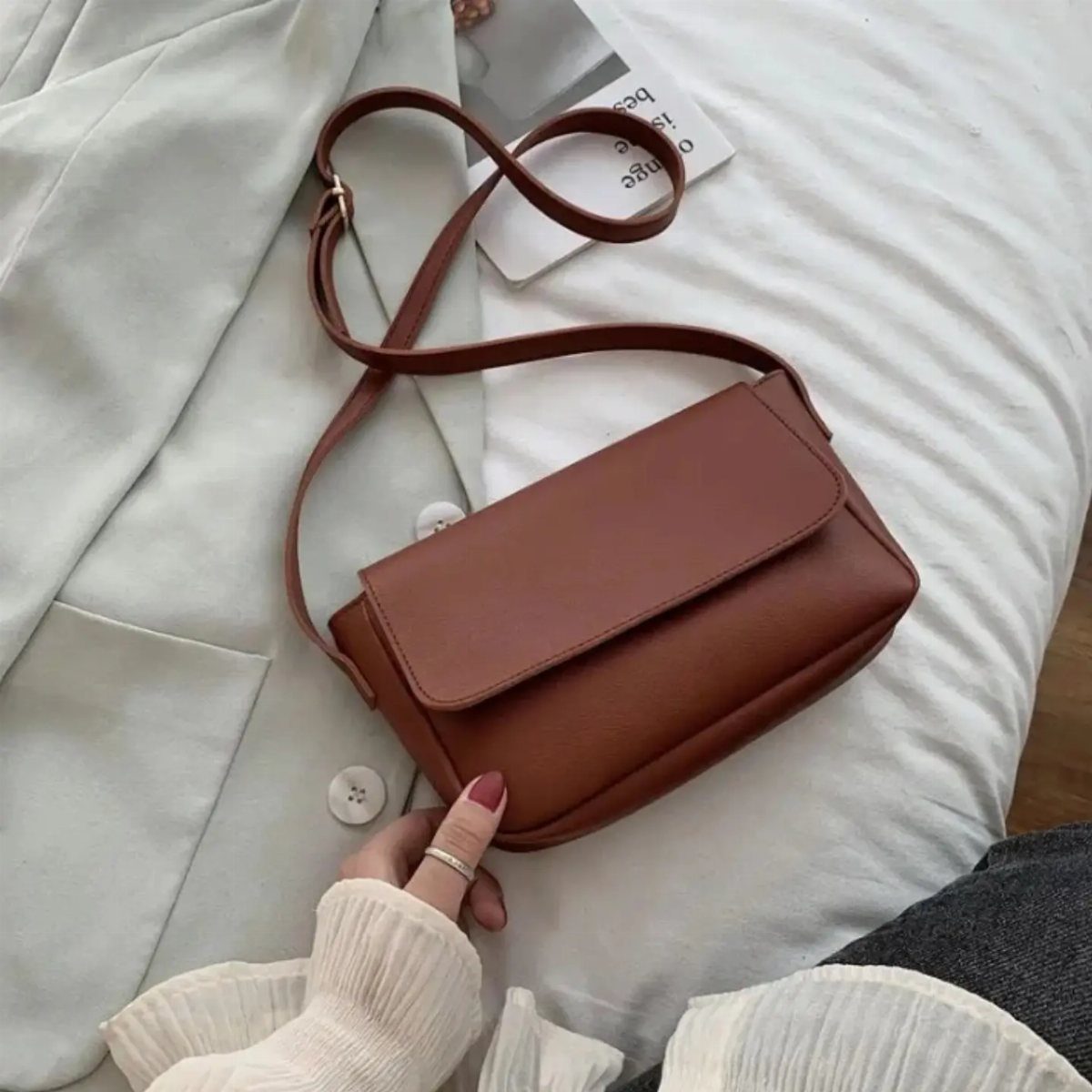 Casual Outfits for Las Vegas: 35 Ideas for Day and Night 16 Brown leather crossbody bag resting on white fabric with a hand touching it.
