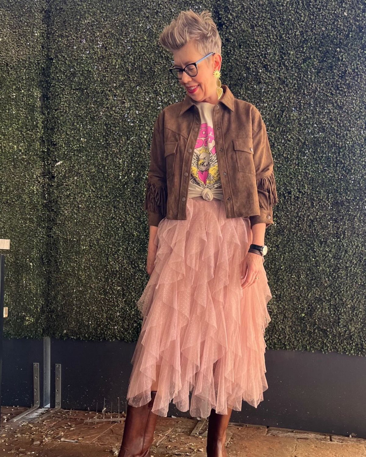 Casual Outfits for Las Vegas: 35 Ideas for Day and Night 24 Woman wearing a brown suede jacket and pink tulle skirt against a green hedge.