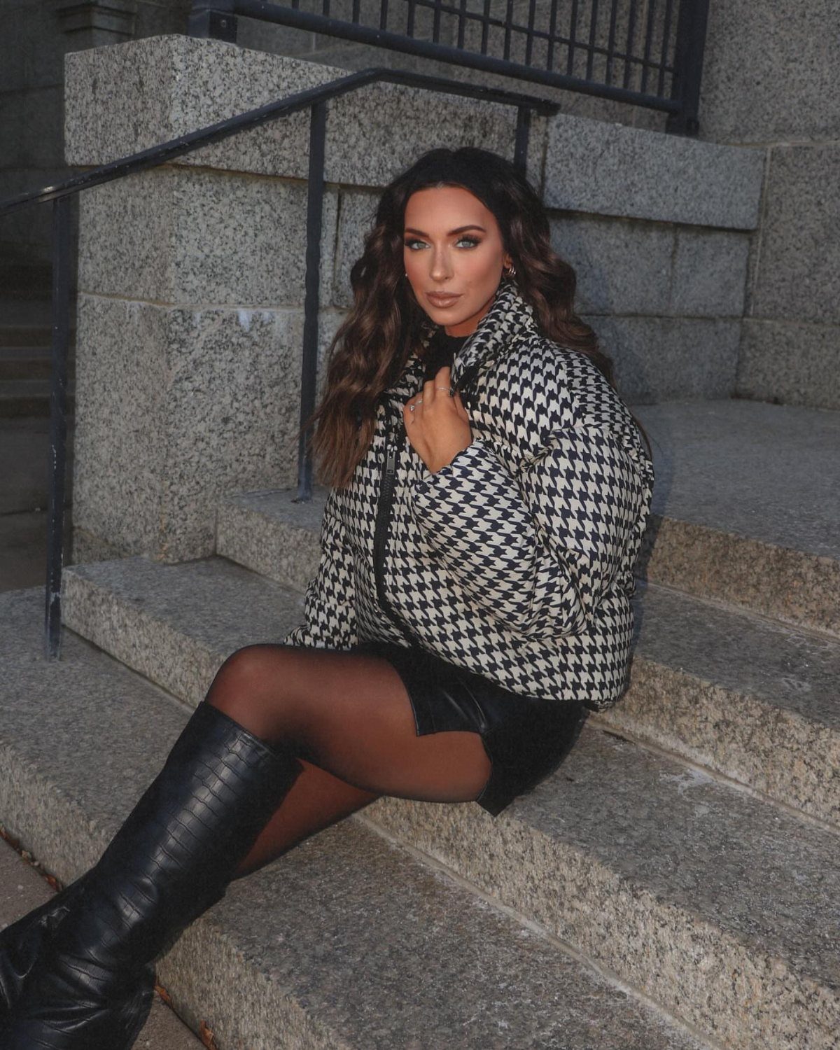 Casual Outfits for Las Vegas: 35 Ideas for Day and Night 31 Woman in houndstooth puffer jacket, leather skirt, and tall black boots on stone steps.