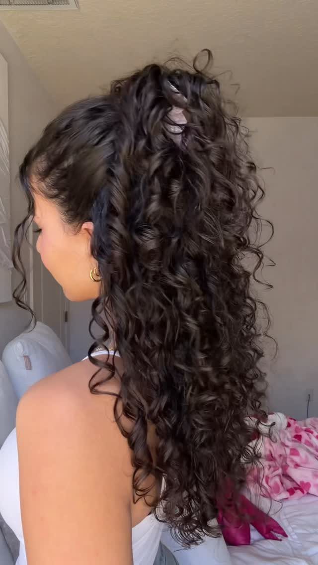 11 Clip Up Hairstyles From French Twists to Half-Up Buns 8 Woman with long dark curly hair in a curly half-up hairstyle.
