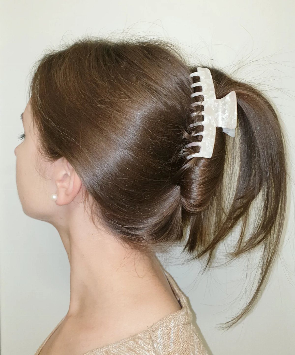 11 Clip Up Hairstyles From French Twists to Half-Up Buns 4 Woman with brown hair in a ponytail secured by a white claw clip
