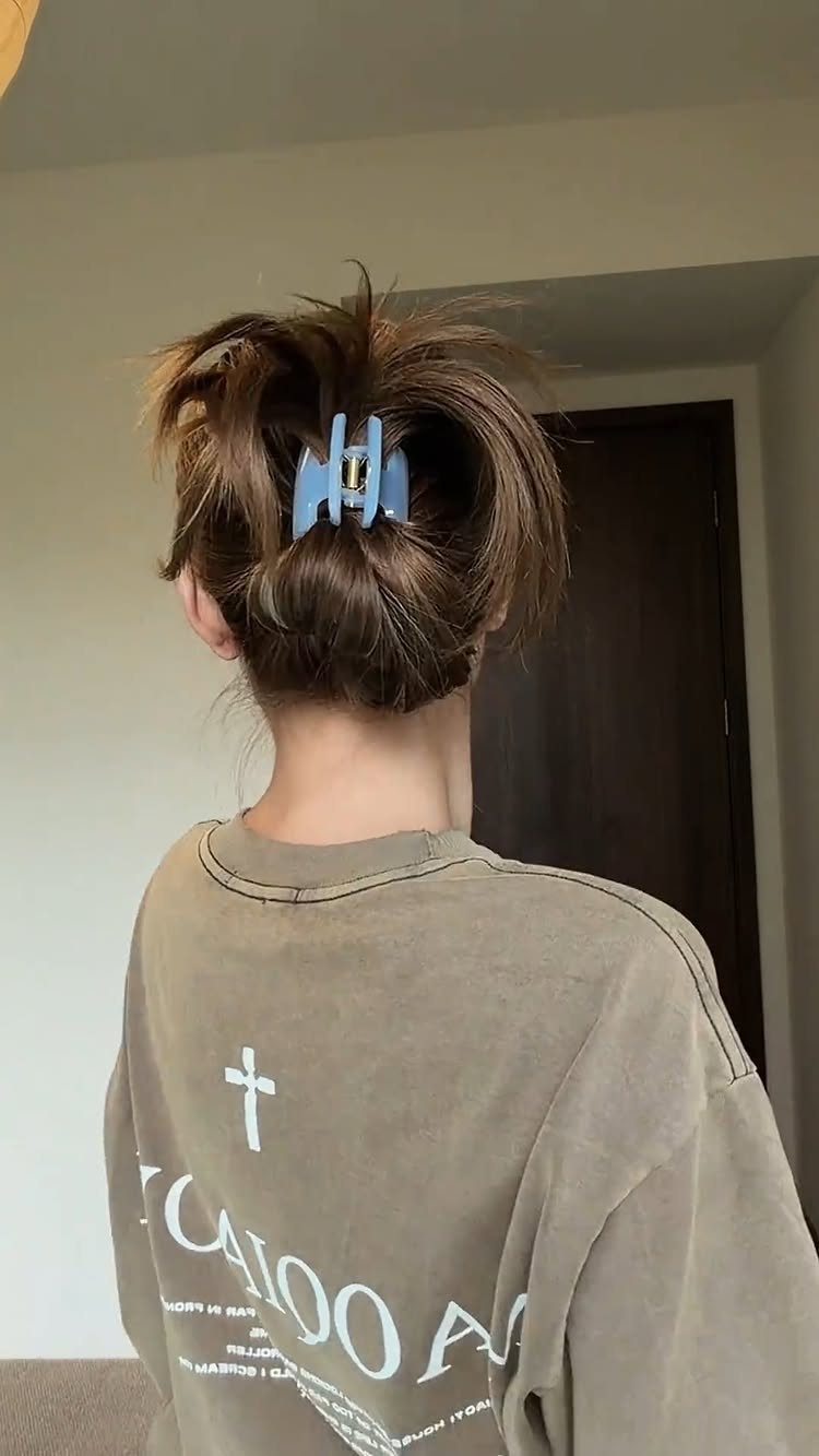 11 Clip Up Hairstyles From French Twists to Half-Up Buns 3 Brown hair styled in a messy bun secured with a blue claw clip.