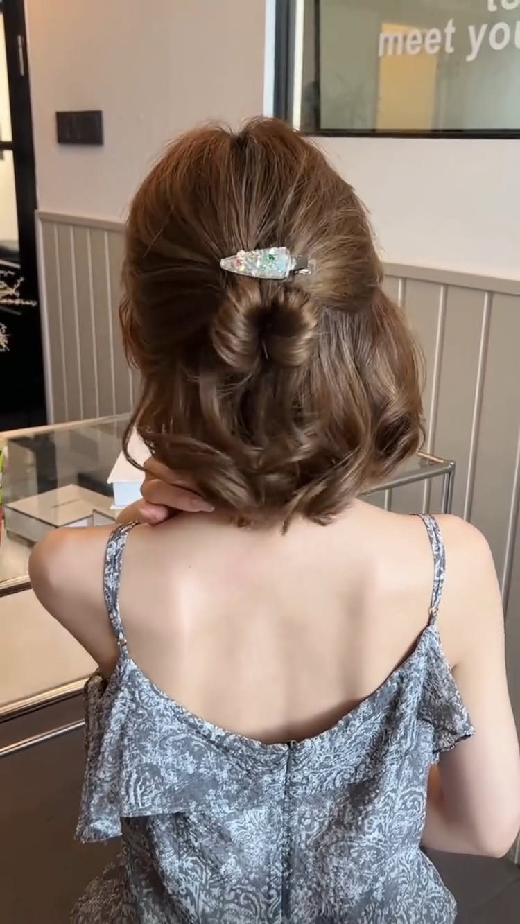 11 Clip Up Hairstyles From French Twists to Half-Up Buns 6 Woman with light brown wavy hair in a messy half-bun with a claw clip