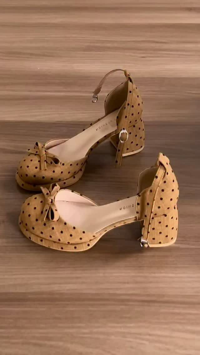 Tan polka-dot closed-toe heels with ankle straps and bows on a wooden floor.