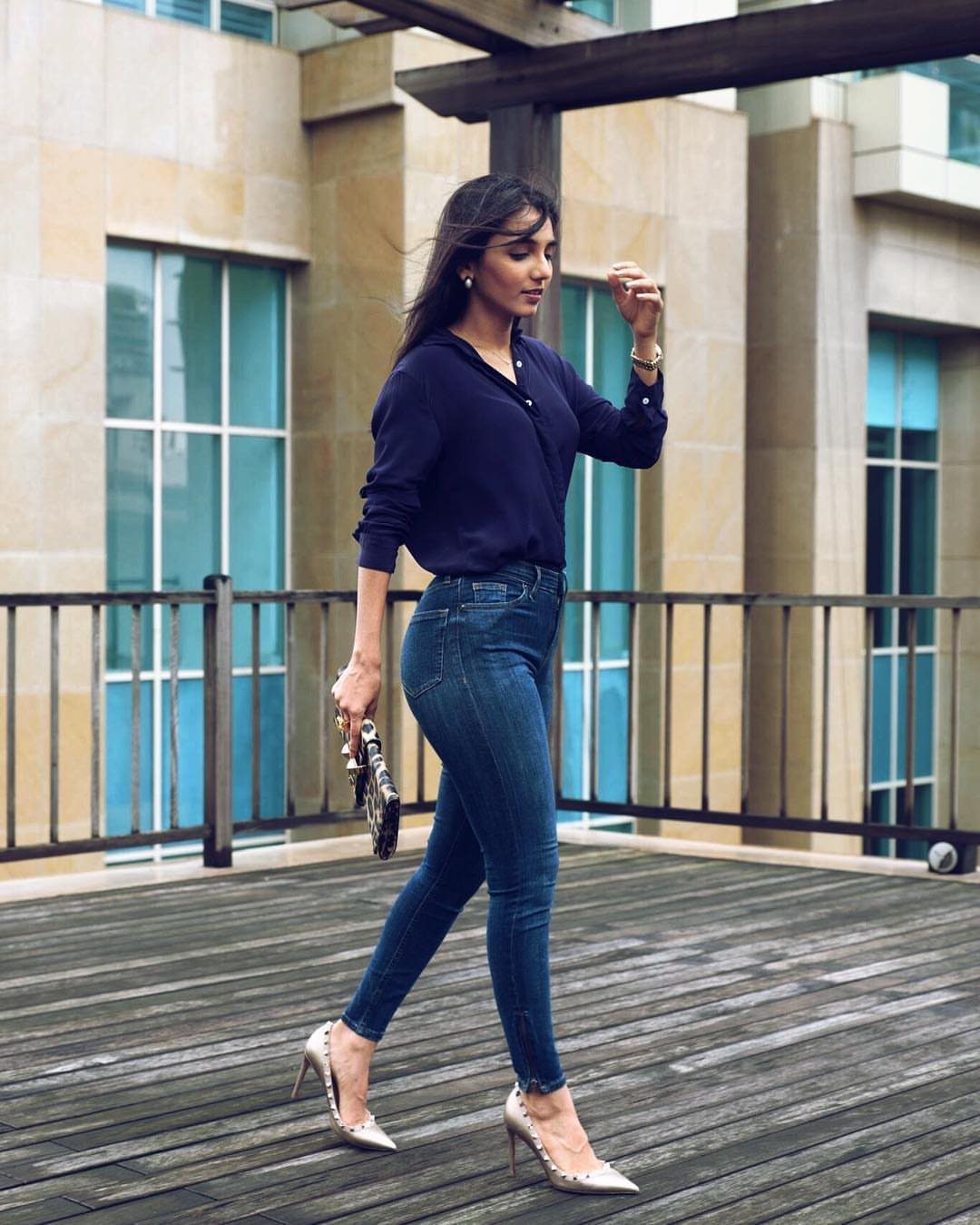 Woman wearing navy blouse, skinny jeans, and silver pointed-toe high heels on a deck.