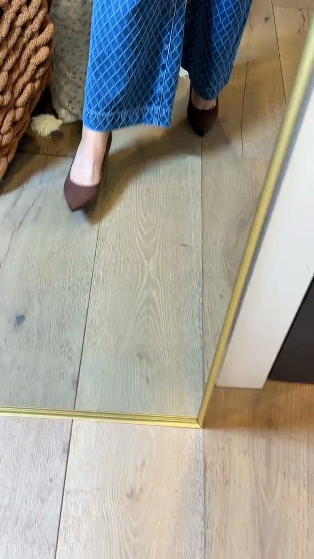 Dark brown pointed-toe pumps worn with blue patterned trousers on a wooden floor.