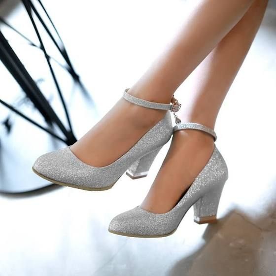 Silver glittery closed-toe pumps with ankle straps and chunky block heels on feet.