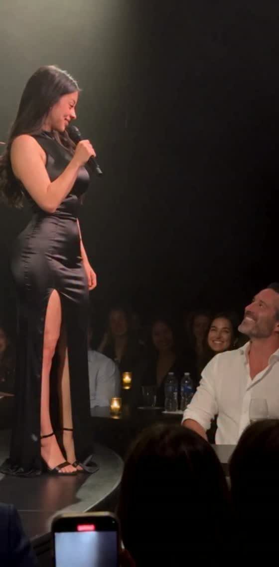 Woman in a long black dress with a thigh slit performing on stage.