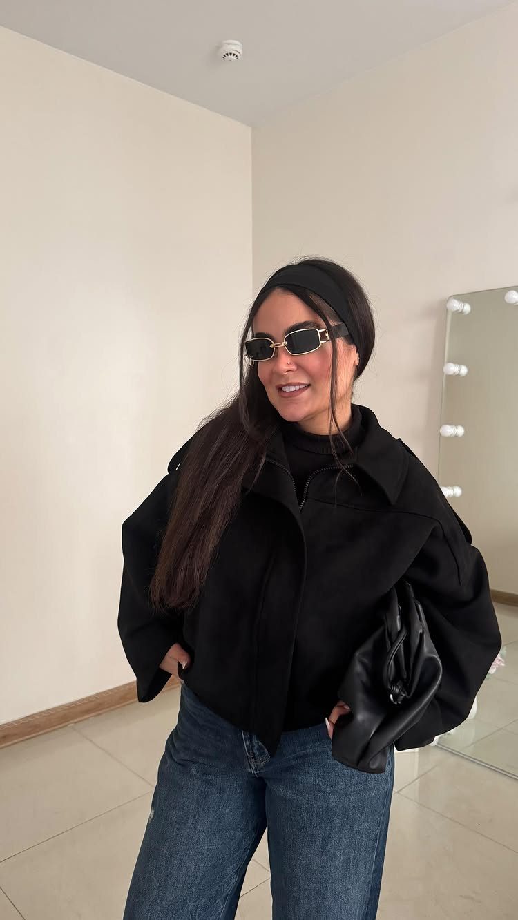 Woman wearing a black oversized jacket, dark blue jeans, and black sunglasses.