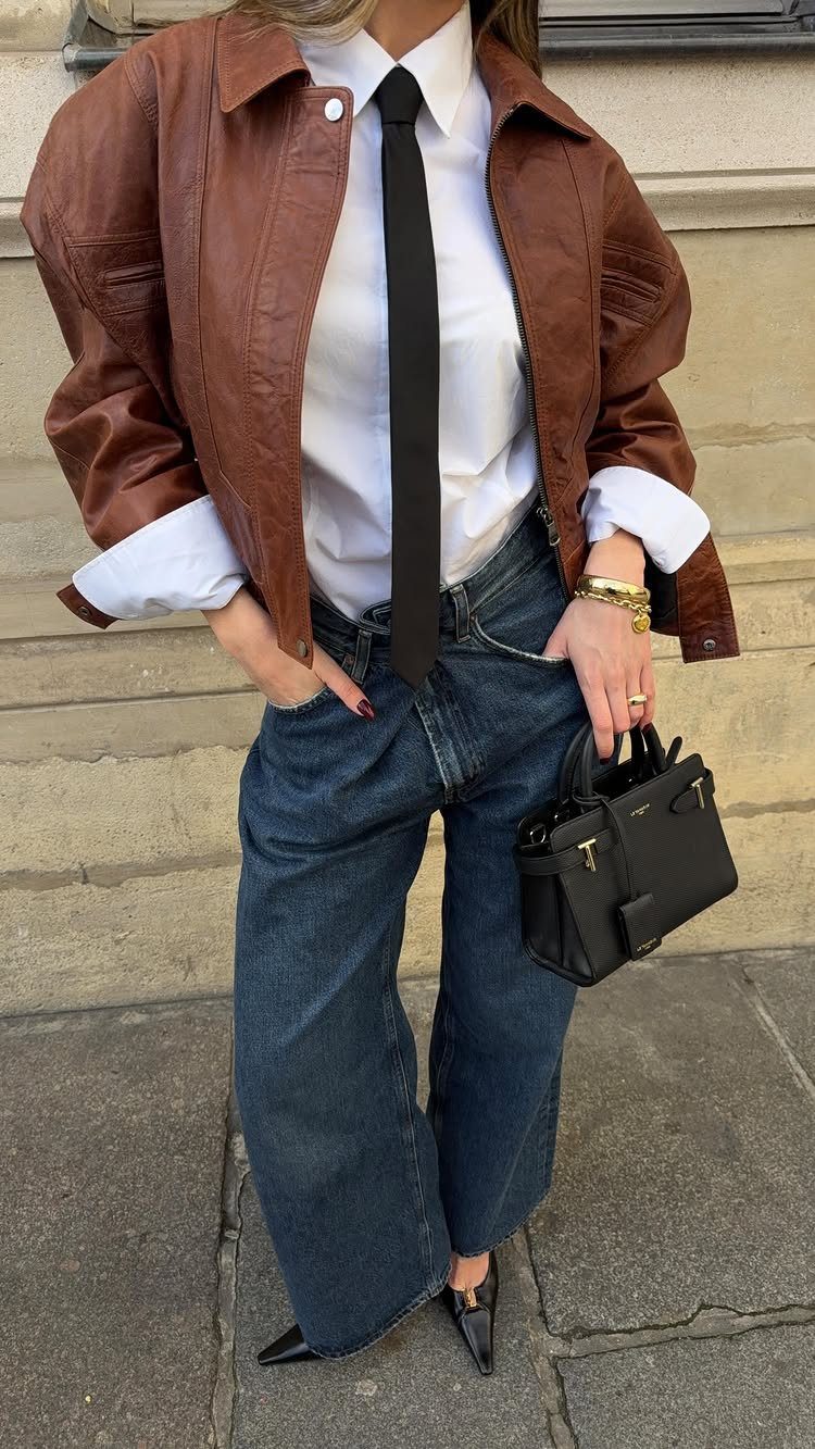 Person wearing a brown leather jacket, white shirt, black tie, and wide-leg jeans.