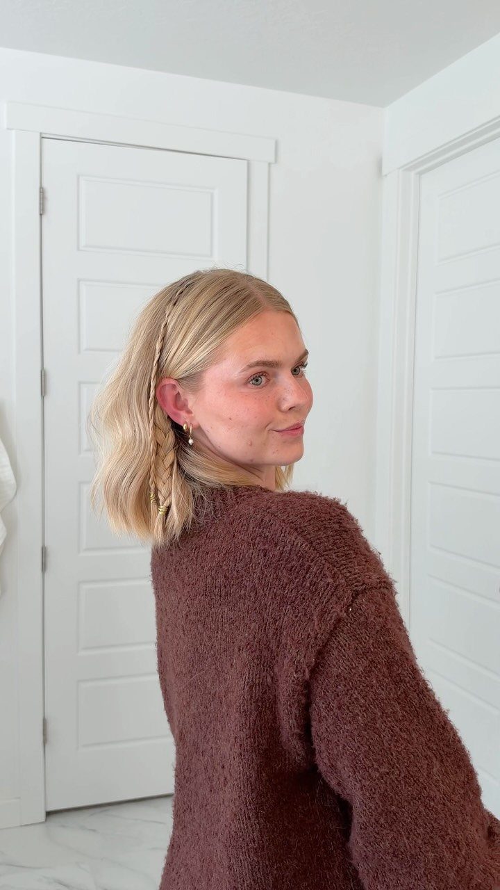 Blonde woman with a braided headband hairstyle wearing a brown fuzzy sweater.