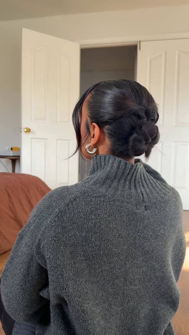 Person with short dark hair styled in a low elegant bun wearing grey sweater.