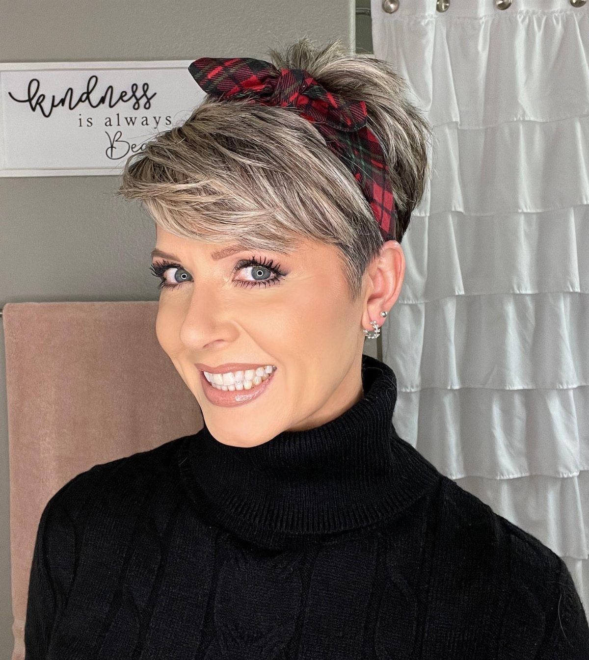 Woman with short blonde hair wearing a red plaid headband and black turtleneck.