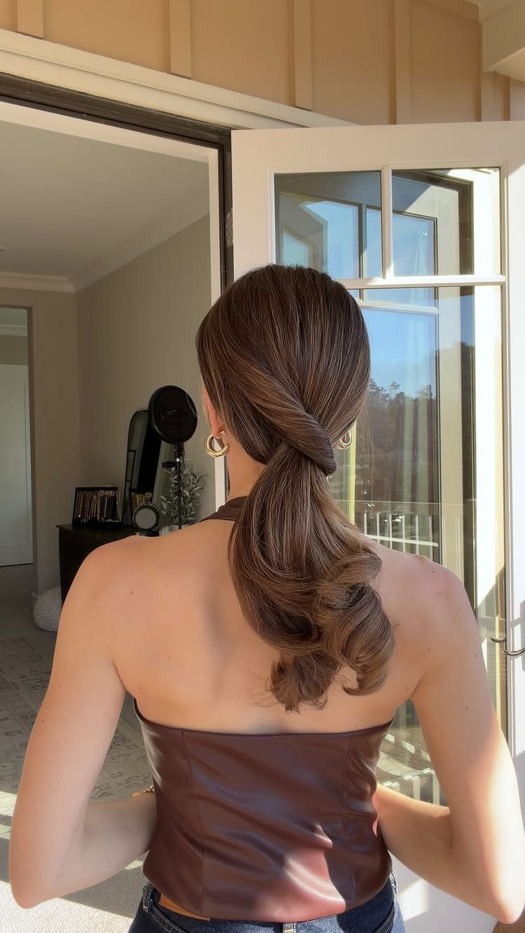 Woman with brown hair in a low twisted ponytail wearing a brown leather top.