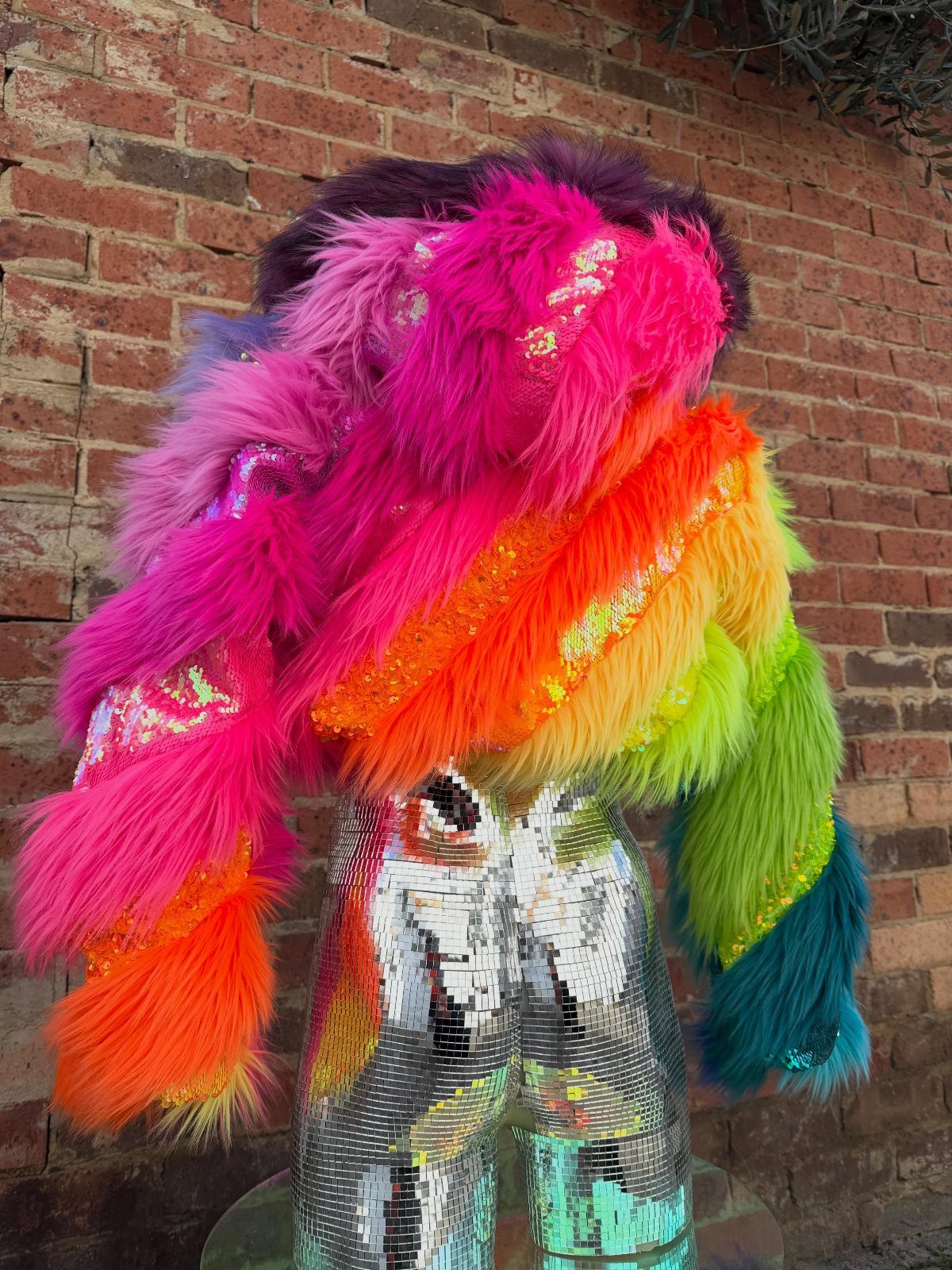 Multi-colored faux fur cropped jacket and silver sequined pants against a brick wall.
