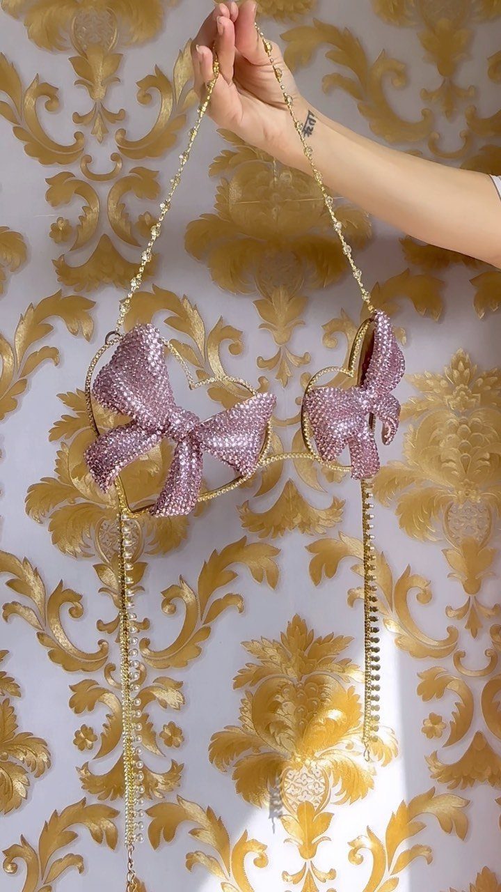 Sparkly purple rhinestone bralette with bow details held against gold damask wallpaper.