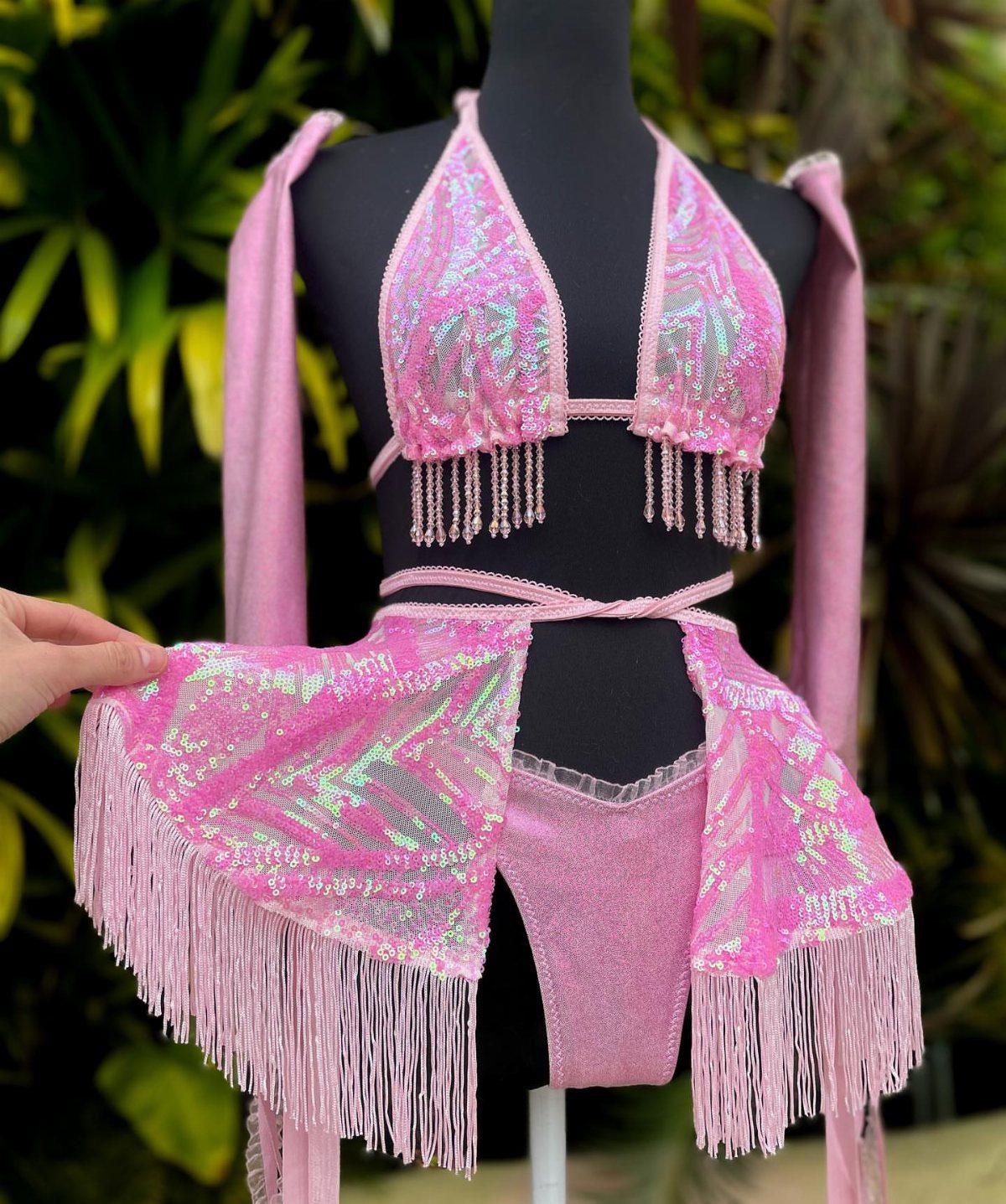 Pink sequined rave outfit with fringe bralette and matching wrap skirt on mannequin.