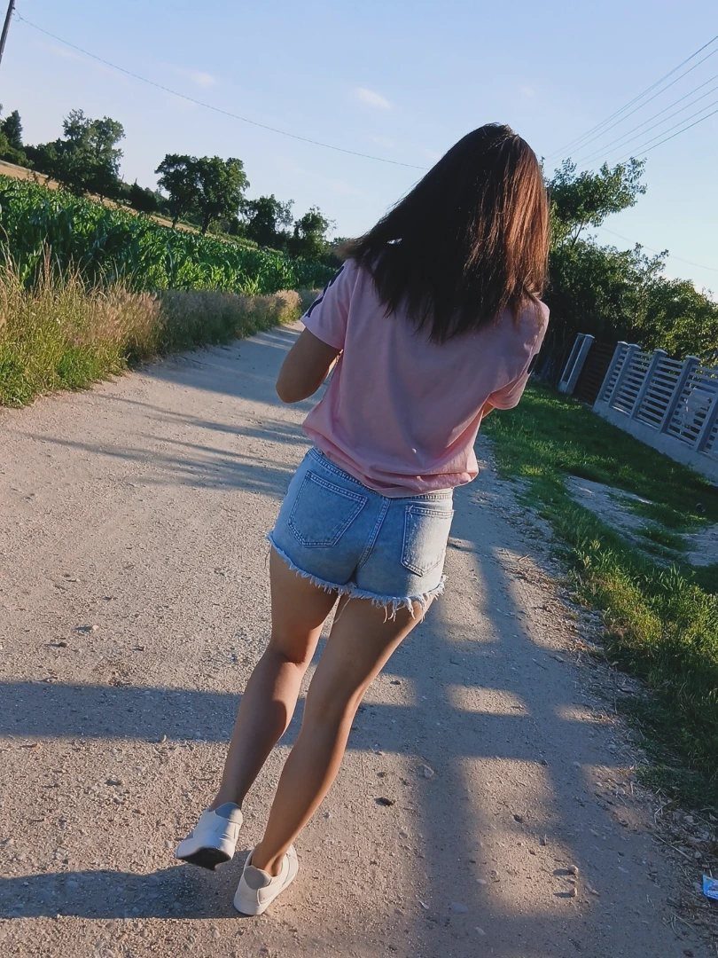 29 Fall Outfits Teens Can Copy, From Grunge to Cowgirl Looks 11 Young woman wearing a pink t-shirt and denim shorts on a sunny dirt path.