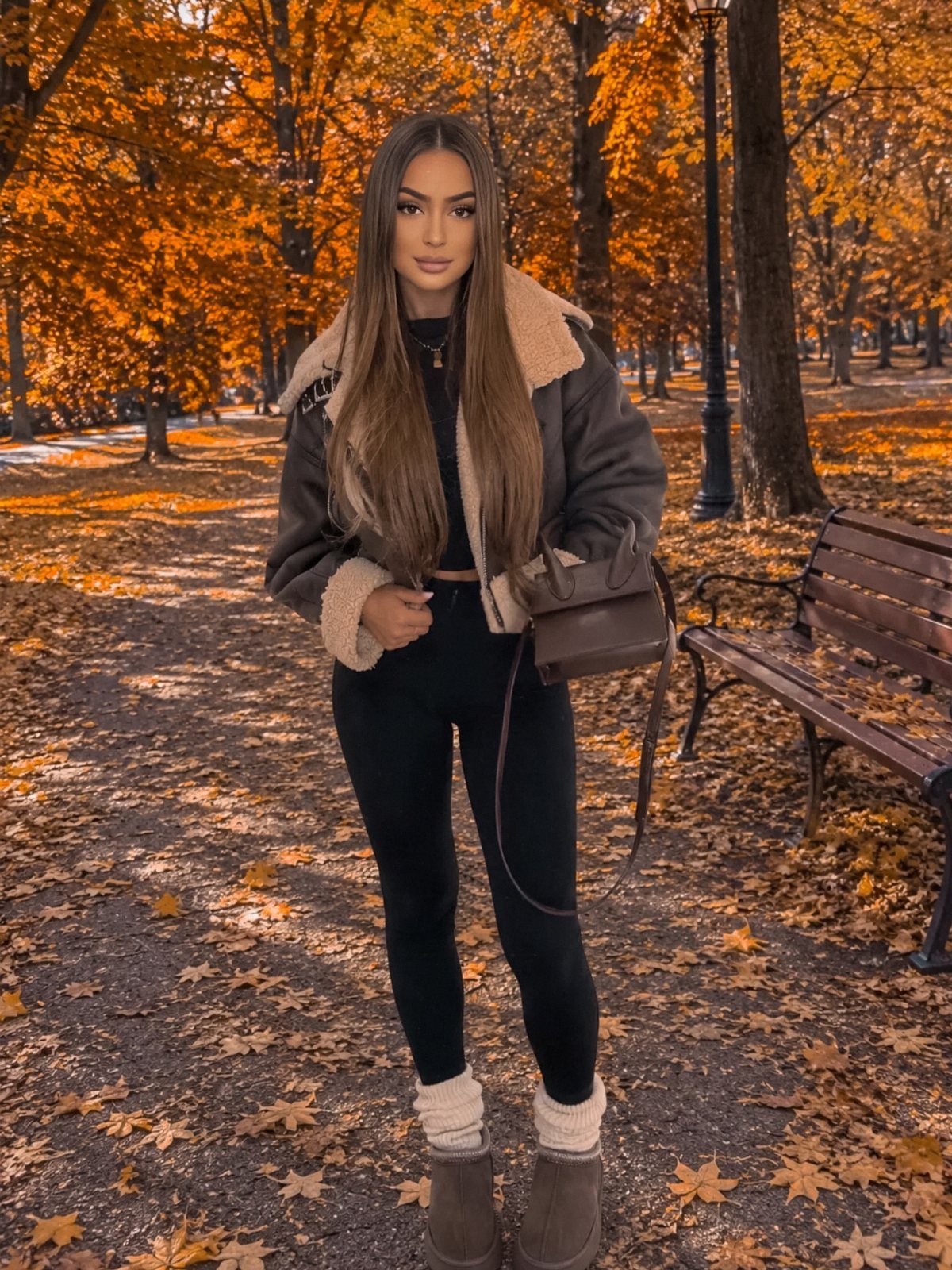 29 Fall Outfits Teens Can Copy, From Grunge to Cowgirl Looks 17 Young woman in a shearling jacket and black leggings posing in an autumn park.