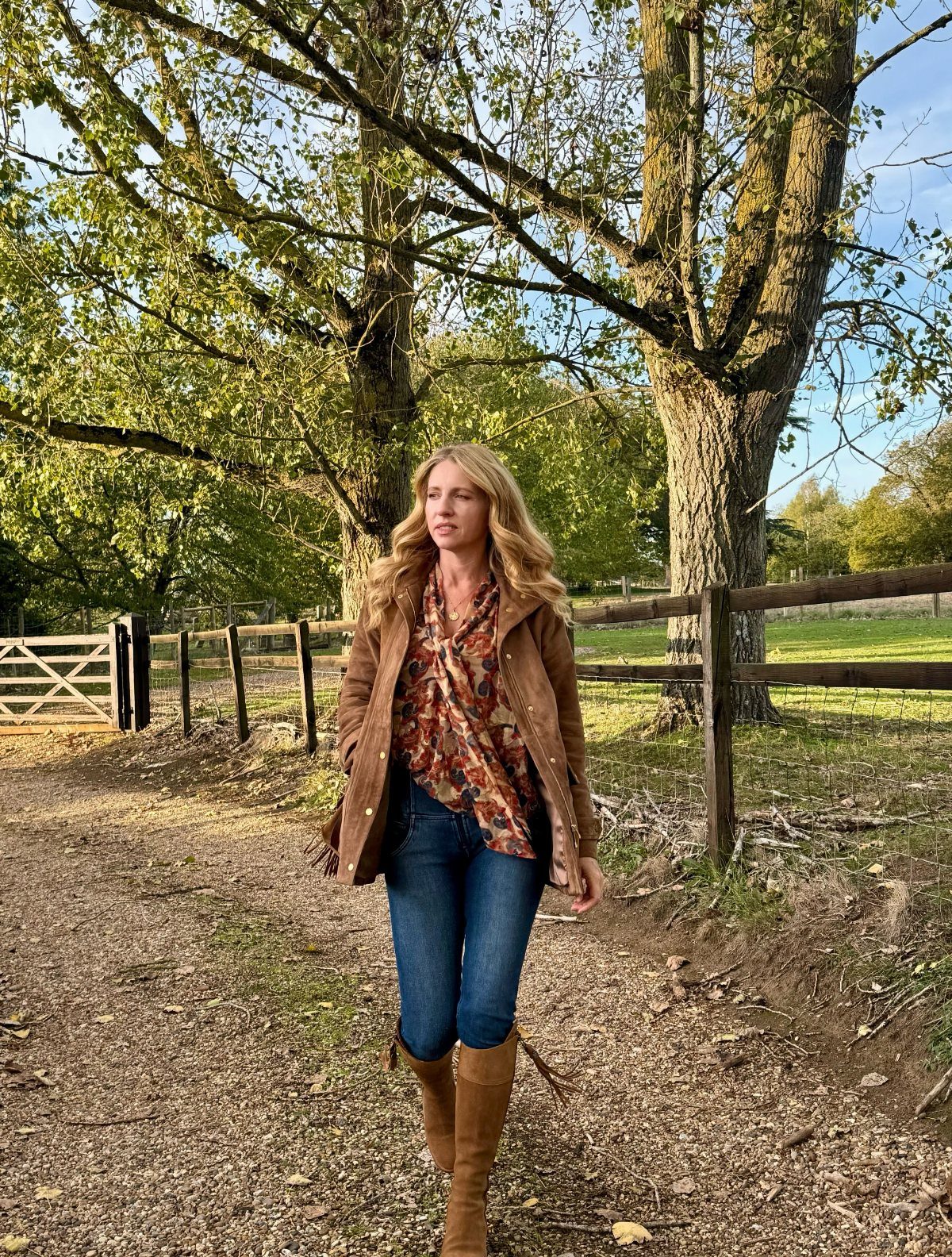 29 Fall Outfits Teens Can Copy, From Grunge to Cowgirl Looks 7 Woman wearing a floral blouse, brown jacket, blue jeans, and brown boots outdoors.