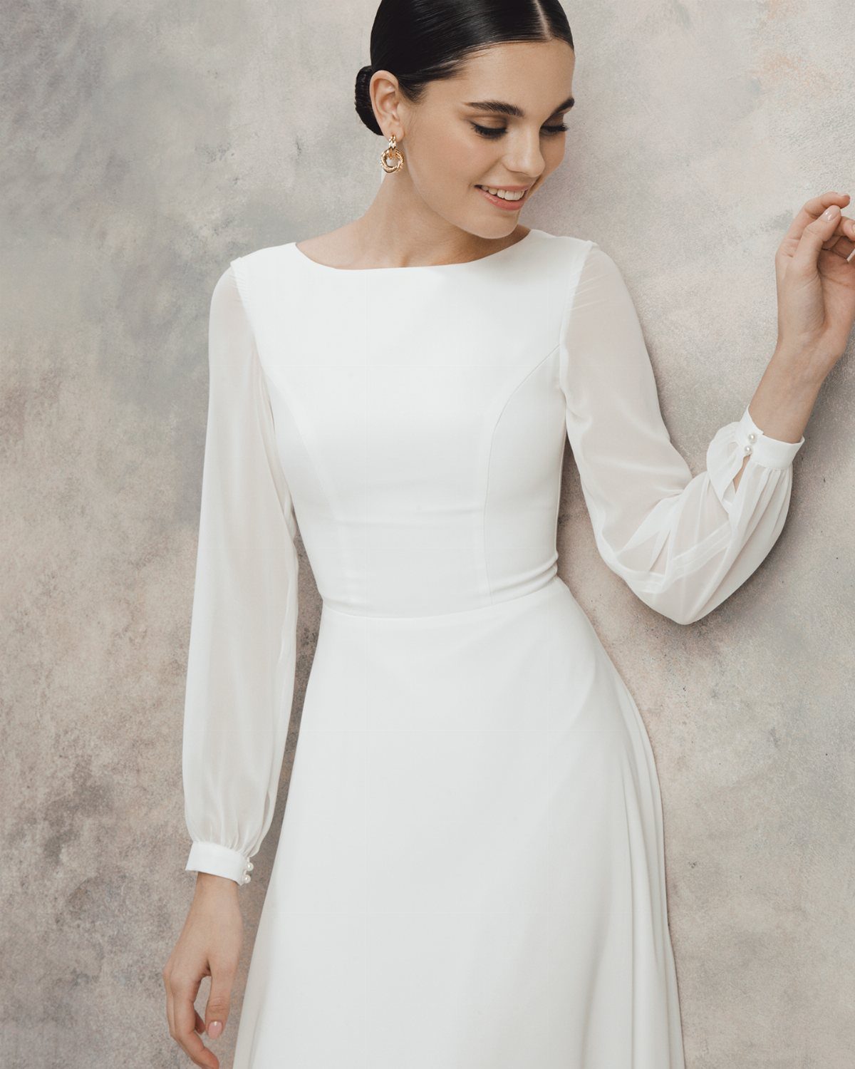 Formal Casual Dresses: 20 Ideas From Shirt Dresses to Velvet 17 Woman wearing a white long-sleeved dress with sheer sleeves against a grey wall.