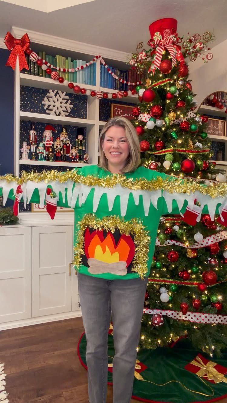 Woman wearing a green Christmas sweater with a fireplace and gold tinsel garland.