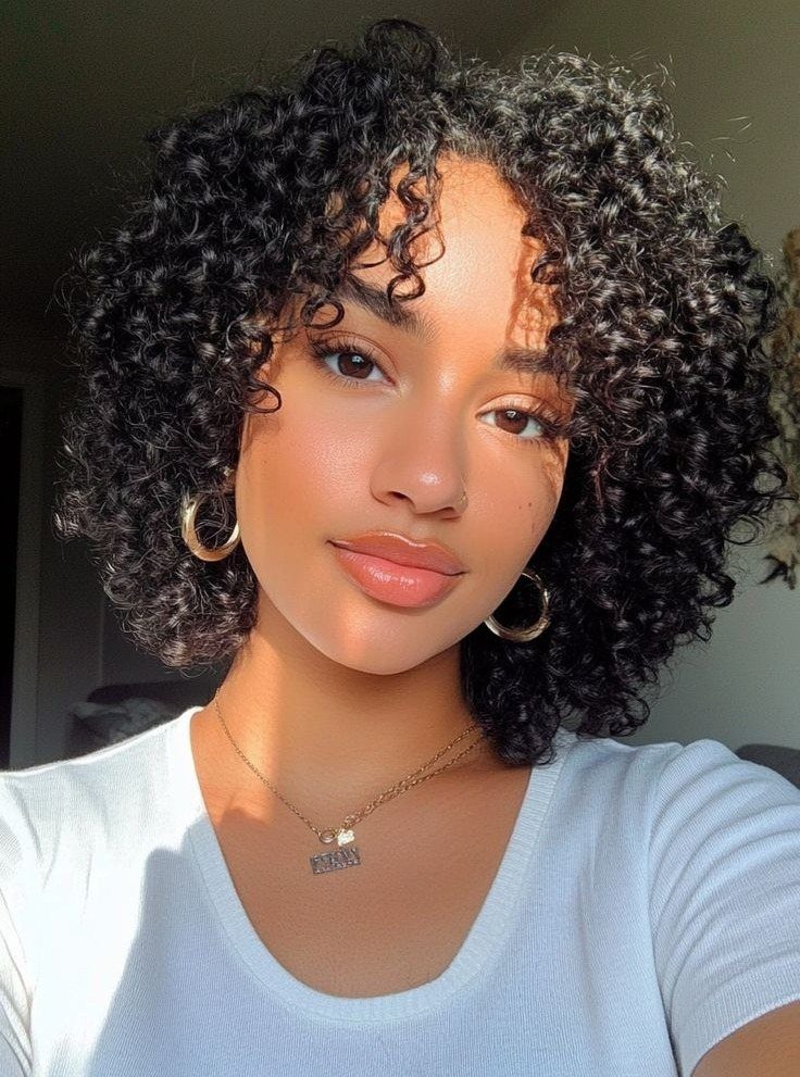 16 Good Hairstyles for Curly Hair, From Pixie to Long Layers 9 Woman with a voluminous dark curly bob hairstyle wearing gold jewelry and white shirt