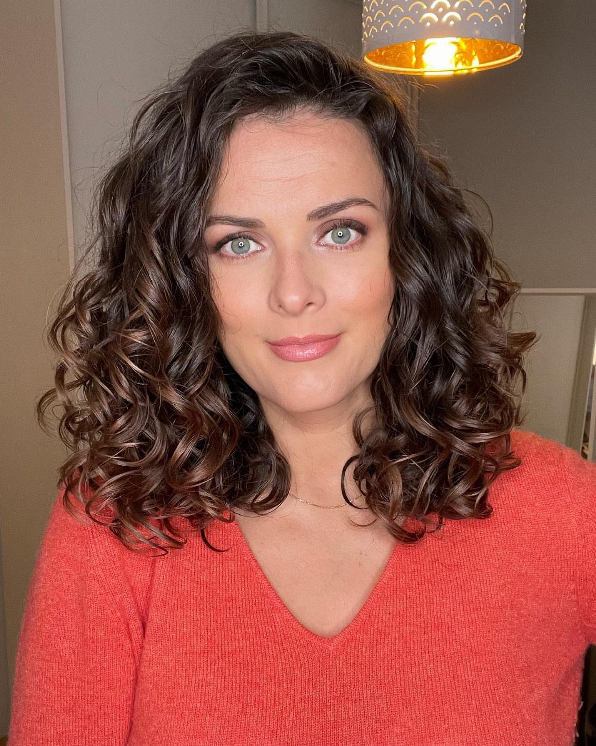 16 Good Hairstyles for Curly Hair, From Pixie to Long Layers 6 Woman with a curly brown layered lob and blue eyes wearing a red sweater.