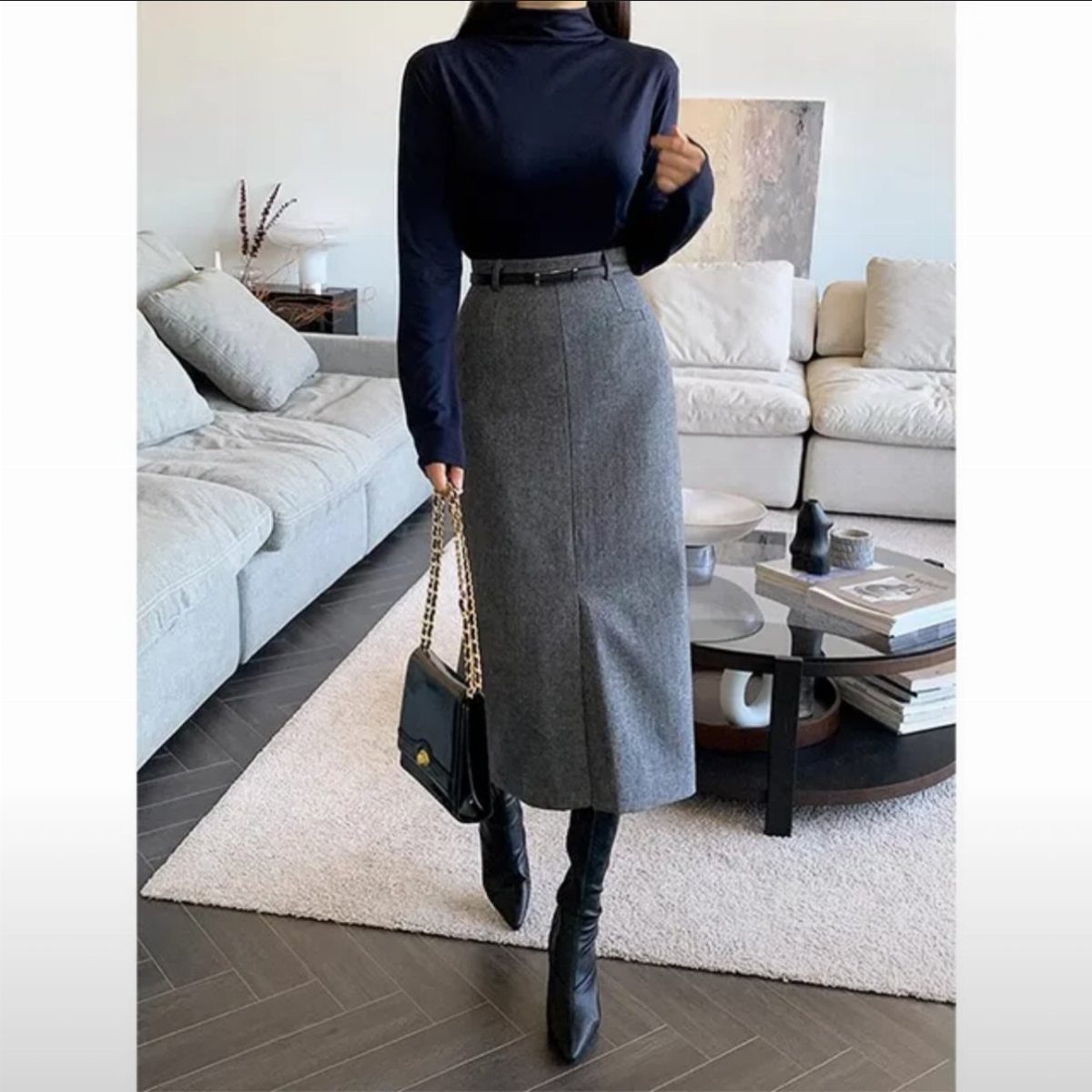 18 Gray Skirt Outfit Ideas From Mini to Maxi and Satin 5 Person wearing a long gray skirt, navy turtleneck, and black boots in a living room.